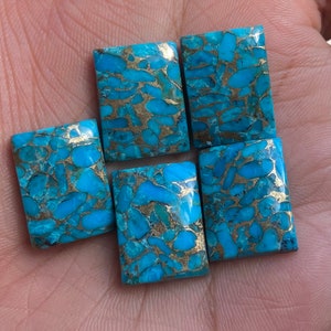 Puede incluir: Cinco cabujones rectangulares de turquesa con motas doradas. Las piedras son de un azul vibrante con un patrón de mármol.