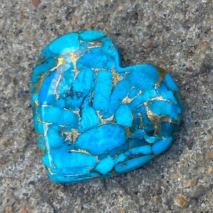 May include: A heart-shaped turquoise stone with gold flecks. The stone is a deep blue colour and has a smooth, polished surface.