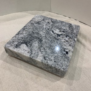 May include: A white and gray granite countertop sample with a smooth, polished surface.