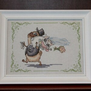 Peut inclure: Une broderie au point de croix encadr&eacute;e en blanc, repr&eacute;sentant une sc&egrave;ne de mariage de dessin anim&eacute; avec un chien brun portant un smoking portant un chat blanc portant une robe blanche et un voile.