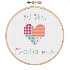 Peut inclure: Un cerceau de broderie blanc avec la phrase "All You Need is Love" brodée en fil noir. Un cœur en patchwork est brodé au centre avec du tissu rose, orange, bleu et blanc.