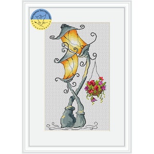 Puede incluir: Un patrón de punto de cruz de una farola caprichosa con una maceta colgante. La farola está hecha de metal gris con una pantalla de lámpara amarilla y naranja. La maceta está llena de flores rojas y rosas.