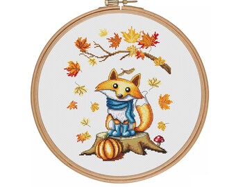 May include: A cross-stitch pattern featuring a cute orange fox wearing a blue scarf and boots, sitting on a tree stump with a pumpkin and a mushroom. Autumn leaves fall from a branch above.