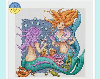 May include: Two mermaids with purple and orange hair are sitting on a blue and green seabed. They are eating fish and drinking from mugs. There are bubbles and seaweed around them.
