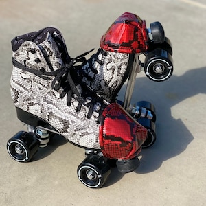 Może przedstawiać: Para rolek z czarno-białym wzorem skóry węża. Rolki mają czarne kółka i sznurowadła, z czerwonymi nakładkami na palce ze wzorem skóry węża. Kołnierz buta ma czarną tkaninę z białym wzorem księżyca i gwiazd.