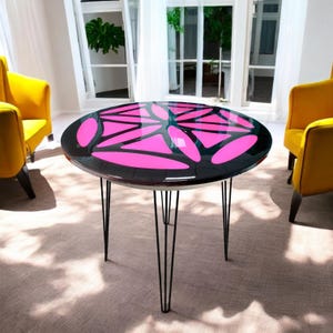 Puede incluir: Una mesa redonda negra y rosa con un dise&ntilde;o geom&eacute;trico en la parte superior. La mesa tiene cuatro patas de horquilla negras.