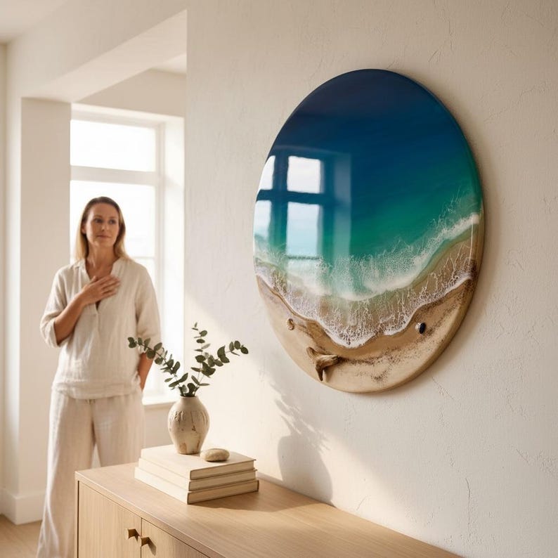 K&ouml;nnte beinhalten: Ein rundes Wandkunstwerk, das eine Strandszene mit blauen und gr&uuml;nen Meereswellen zeigt, die auf einen sandigen Strand treffen. Das Kunstwerk ist an einer wei&szlig;en Wand befestigt und hat eine gl&auml;nzende Oberfl&auml;che. Das Kunstwerk hat einen Durchmesser von etwa 61 cm.