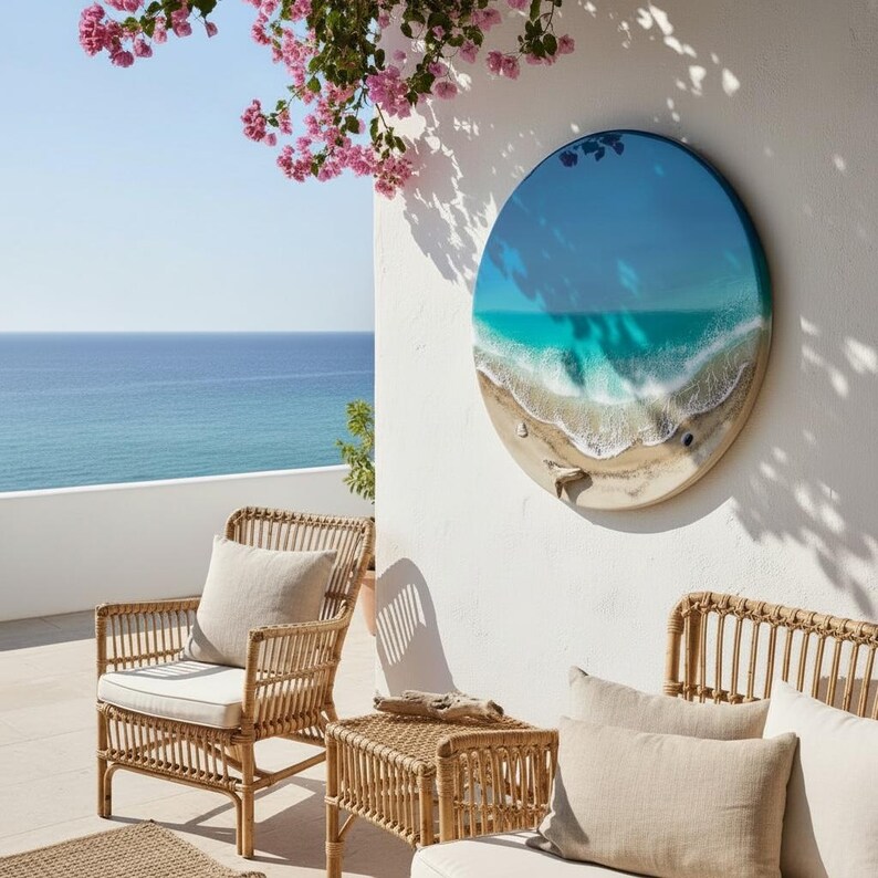 K&ouml;nnte beinhalten: Runde Wandkunst mit einer Strandlandschaft mit blauem und t&uuml;rkisfarbenem Wasser, wei&szlig;en Wellen und einem sandigen Ufer. Das Kunstwerk h&auml;ngt an einer wei&szlig;en Wand, mit Korbm&ouml;beln und Meerblick im Hintergrund.