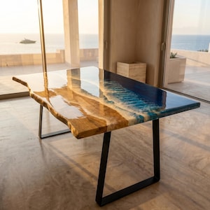May include: A rectangular dining table featuring a natural live-edge wood slab combined with a glossy blue resin section that mimics ocean waves with white foam detailing. The table is supported by two black metal U-shaped legs.