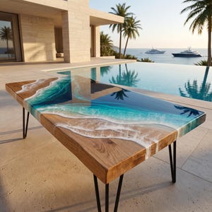 Può includere: Un tavolino rettangolare in legno con un inserto in resina che imita una costa con acqua turchese e blu profondo, onde di schiuma bianca e una texture di sabbia, sostenuto da quattro sottili gambe a forcina in metallo nero.