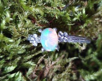 May include: A silver ring with a delicate twig design and a white opal gemstone. The ring is adorned with small flower accents.