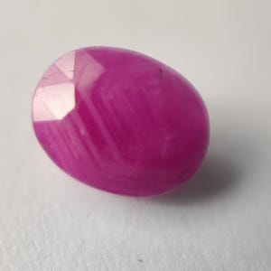 Op de afbeelding: Een levendige roze ovaalvormige edelsteen met een facetgeslepen vorm. De edelsteen heeft een gestreept patroon en een glanzende afwerking.