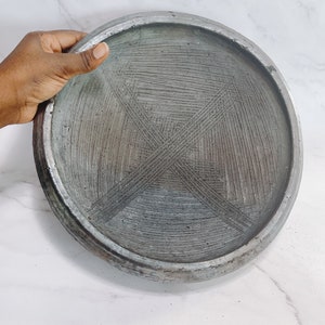 May include: A round, gray, ceramic plate with a textured surface. The plate has a raised rim and a design of criss-crossing lines.