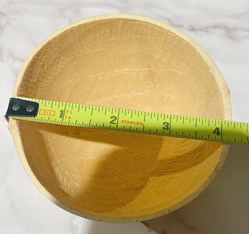 May include: A light brown, round, gourd bowl with a diameter of approximately 3 inches. The bowl is made from a natural material and has a smooth, slightly textured surface.