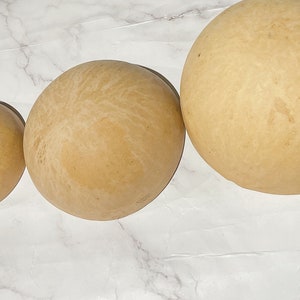 May include: Three round, beige gourds of varying sizes, arranged in a row on a white marble surface.