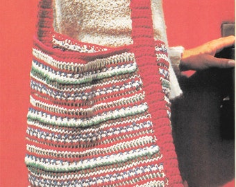 May include: A crocheted shoulder bag with a red strap and a striped pattern in red, white, green, and blue. The bag is worn over the shoulder. The person is wearing a white sweater.