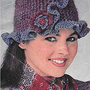 May include: A crocheted cloche hat in shades of purple and blue, adorned with floral embellishments. The hat features a ruffled brim and is designed with a vintage aesthetic, suitable for various occasions.