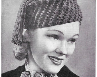 May include: A black and white photo of a woman wearing a crocheted hat with a tassel. The hat is a dark color and has a textured design. The woman is smiling and looking to the side.