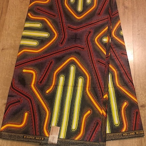 May include: A black fabric with a geometric pattern of yellow, orange, and red lines on a black background. The fabric has a white label that says "Super Wax" and "Holland 18200".