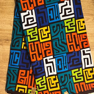 May include: A colourful fabric with a geometric pattern of interlocking squares and lines in shades of orange, blue, green, yellow, and white on a black background. The fabric has a label with the text "TARGET 2752812".
