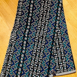 May include: A fabric with a geometric pattern in shades of blue, green, white, and black. The pattern features repeating diamonds, triangles, and lines.
