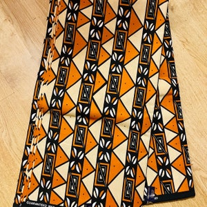 May include: A folded fabric with a geometric pattern in orange, black, and white. The fabric has a "Guaranteed Wax" label and a "101" label.