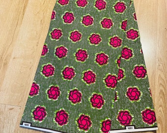 May include: A green and pink fabric with a repeating pattern of stylized pink flowers. The fabric has a white stripe running horizontally across the fabric. The fabric is labeled "1051" in the bottom left and right corners. The fabric is labeled "Guaranteed" in the bottom right corner.