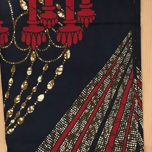 May include: A dark blue fabric with a red and gold pattern. The pattern features a chandelier with candles and a repeating geometric design.