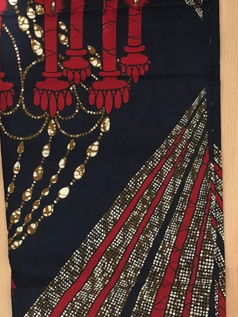May include: A dark blue fabric with a red and gold pattern. The pattern features a chandelier with candles and a repeating geometric design.