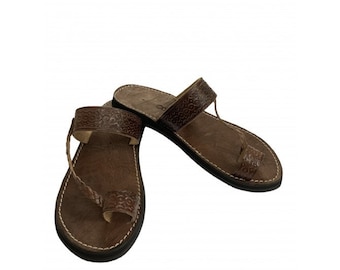 Peut inclure: Une paire de sandales en cuir marron avec une sangle tissée et un motif décoratif. Les sandales ont une sangle de toe thong.