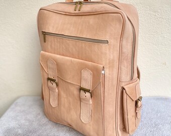 May include: A light brown leather backpack with multiple pockets and buckles. The backpack has a top zipper closure and a large front pocket with two buckles.