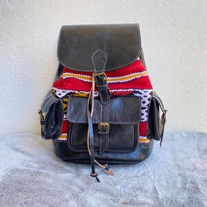 May include: A black leather backpack with a colourful woven pattern on the front. The backpack has two large pockets and a smaller pocket on the side.