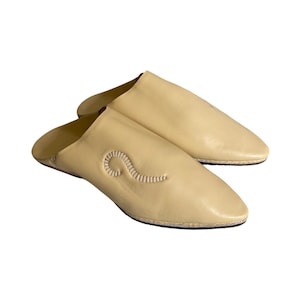 May include: A pair of light yellow leather slippers with a pointed toe and a decorative stitch design. The slippers are made of soft leather and have a comfortable fit.
