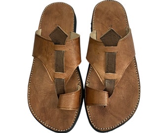 Peut inclure: Une paire de sandales en cuir marron avec un design simple. Les sandales ont une sangle qui passe sur l'orteil et une petite sangle qui passe autour de la cheville.