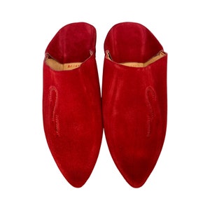 Puede incluir: Un par de zapatillas de piel de gamuza roja con punta y un diseño sencillo. Las zapatillas tienen la parte trasera cerrada y un estilo de deslizamiento.