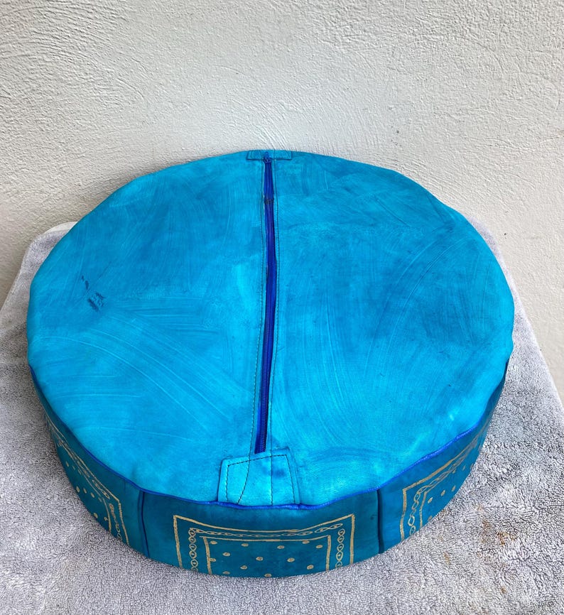 May include: A round blue leather pouf with a zipper closure and a gold bandana pattern around the bottom.