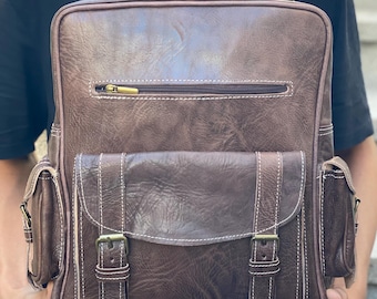 May include: A brown leather backpack with multiple pockets and buckles. The backpack has a zippered closure and a top handle.