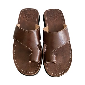 Op de afbeelding: Een paar bruine leren teenslippers met een teenlus. De slippers hebben een eenvoudig ontwerp en zijn gemaakt van hoogwaardig leer.