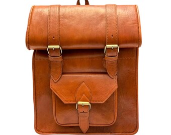 以下が含まれることがあります： フラップ留めと2つのバックルが付いた茶色の革製バックパック。バックパックには、バックル留めのある大きなフロントポケットがあります。