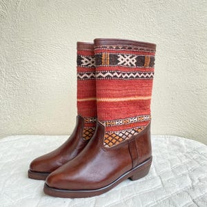 May include: Brown leather boots with a red, orange, and black patterned fabric shaft.