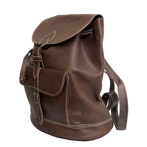 Könnte beinhalten: Ein brauner Lederrucksack mit Klappenverschluss und Vordertasche. Die Tasche hat weiße Nähte und verstellbare Träger. Der Rucksack ist im klassischen Vintage-Stil gehalten.