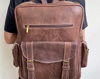 May include: A brown leather backpack with multiple pockets and buckles. The backpack has a top handle and adjustable shoulder straps.
