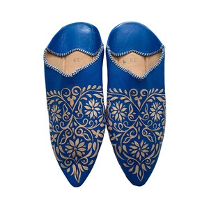Puede incluir: Un par de zapatillas de cuero azul con punta puntiaguda y bordado floral dorado intrincado.