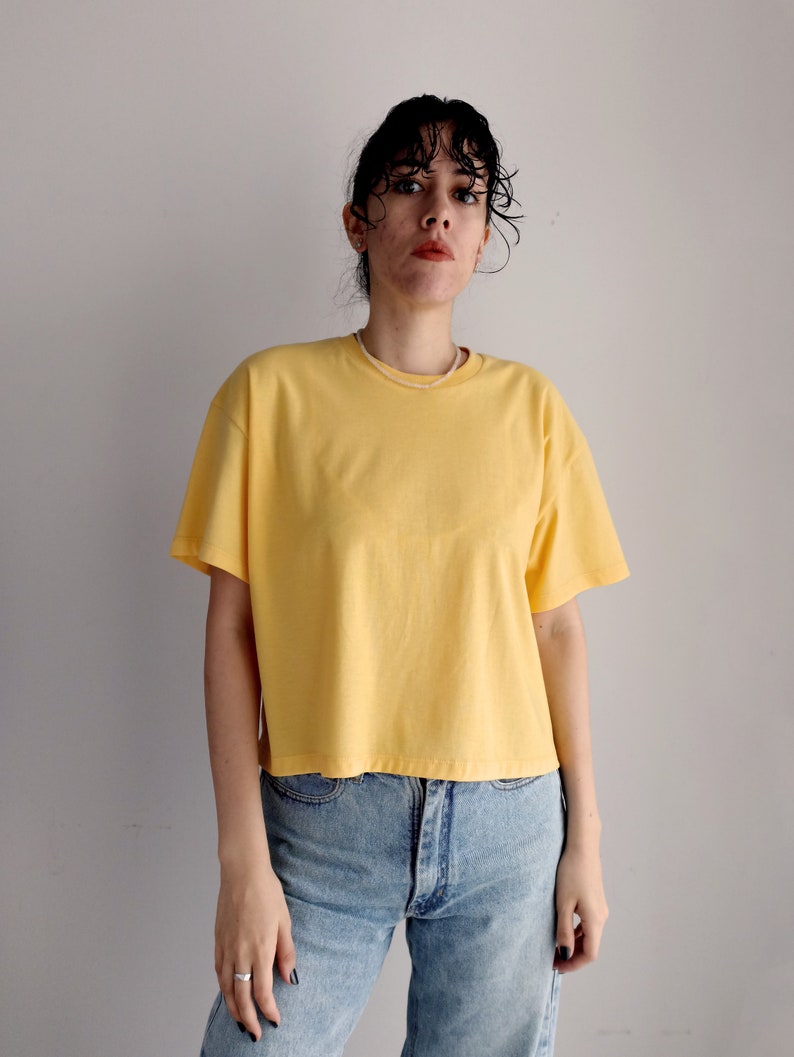 May include: A woman wearing a yellow cropped t-shirt and blue jeans.