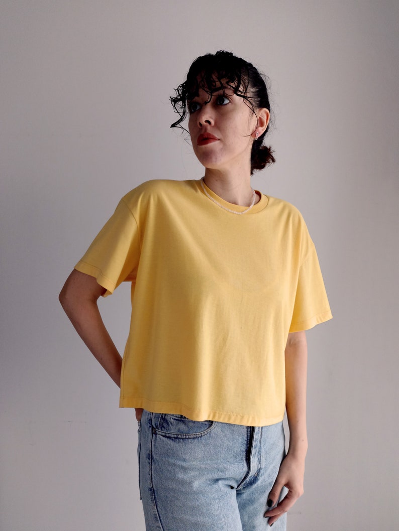 May include: A woman wearing a yellow short-sleeved t-shirt and light blue jeans.