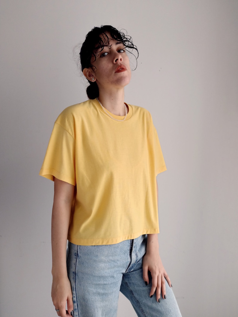 May include: A woman wearing a yellow cropped t-shirt and blue jeans.