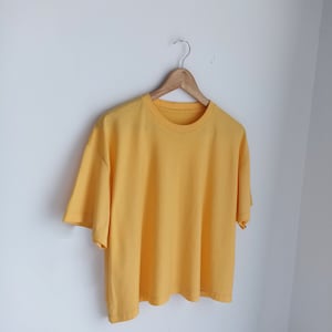 May include: A yellow short-sleeved t-shirt hanging on a wooden hanger against a white background.