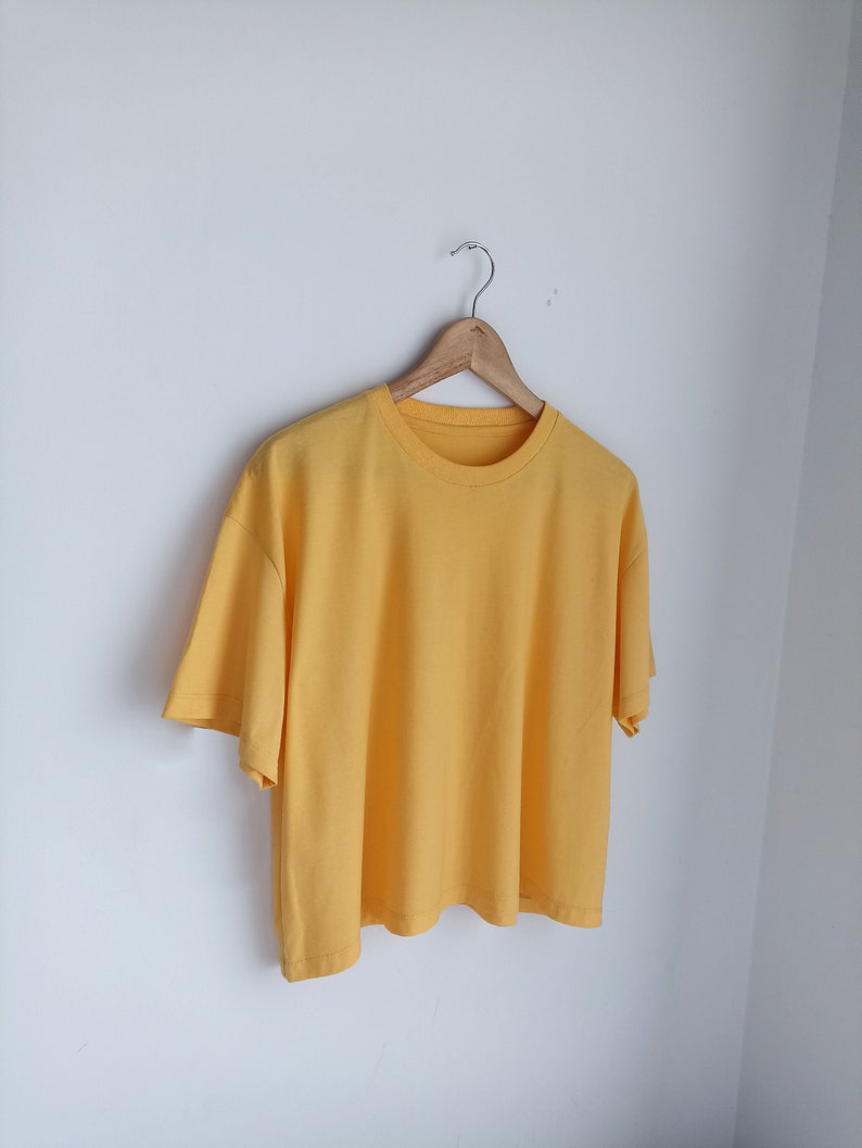 May include: A yellow short-sleeved t-shirt hanging on a wooden hanger against a white background.