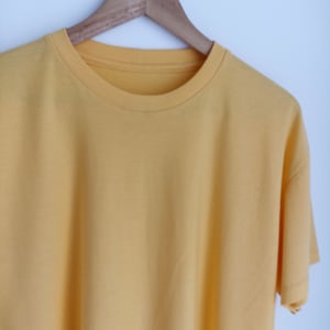 May include: A plain yellow t-shirt hanging on a wooden hanger against a white background.
