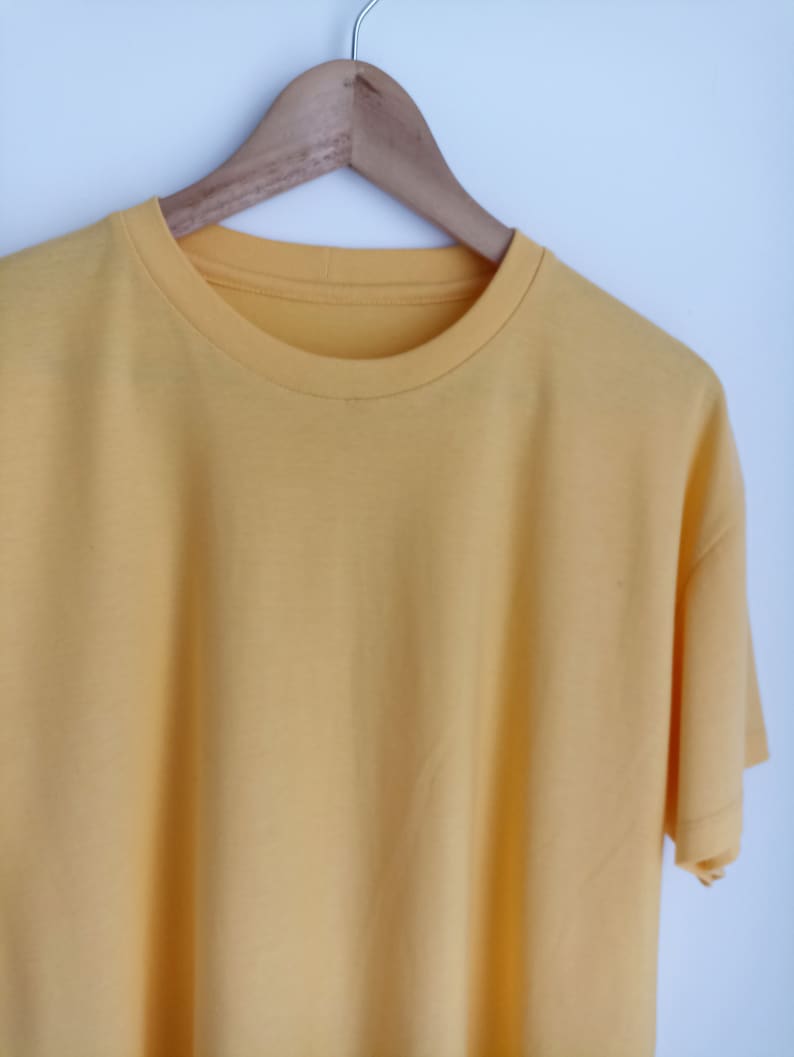 May include: A plain yellow t-shirt hanging on a wooden hanger against a white background.